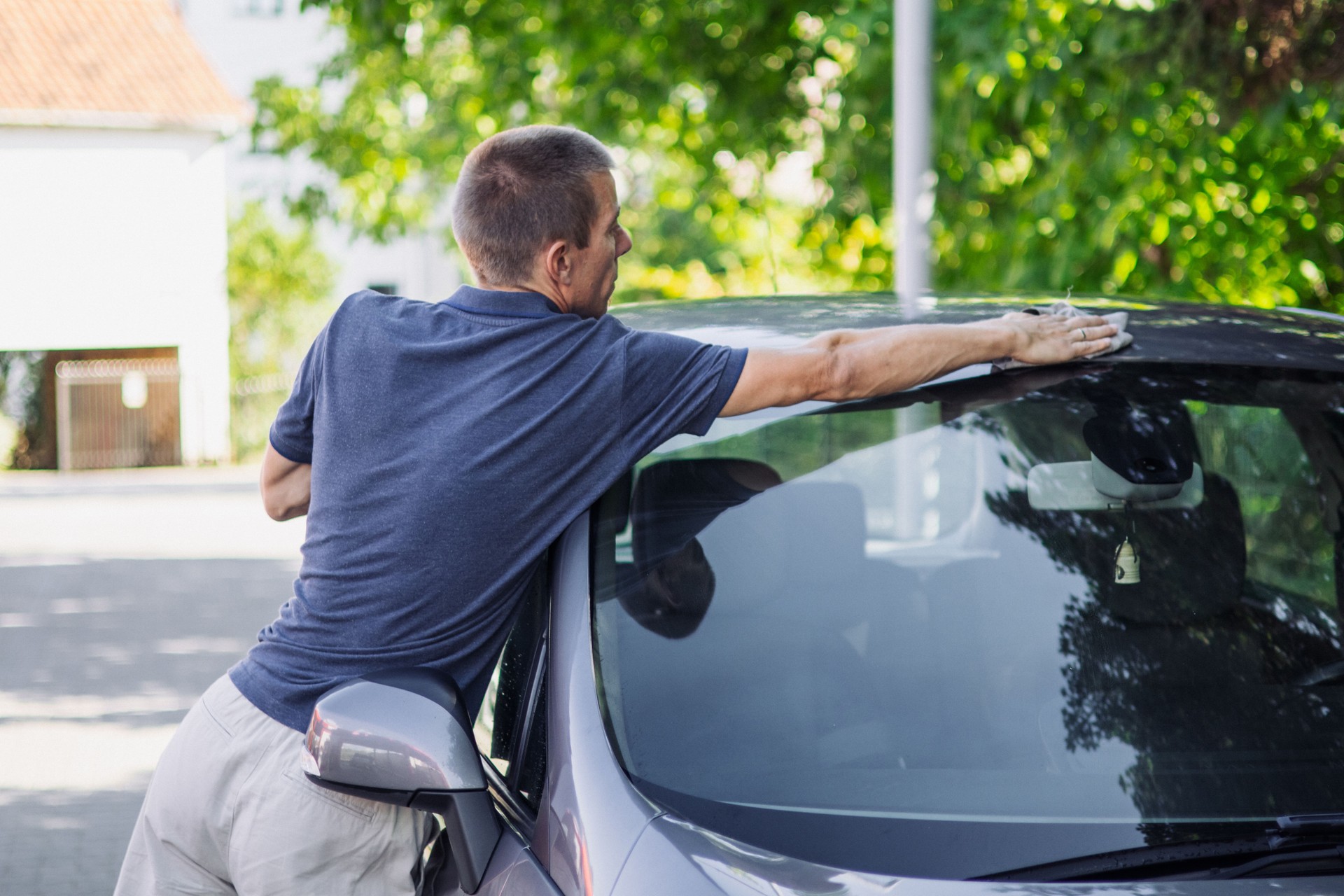 Man is cleaning, wiping and polishing exterior of his car.