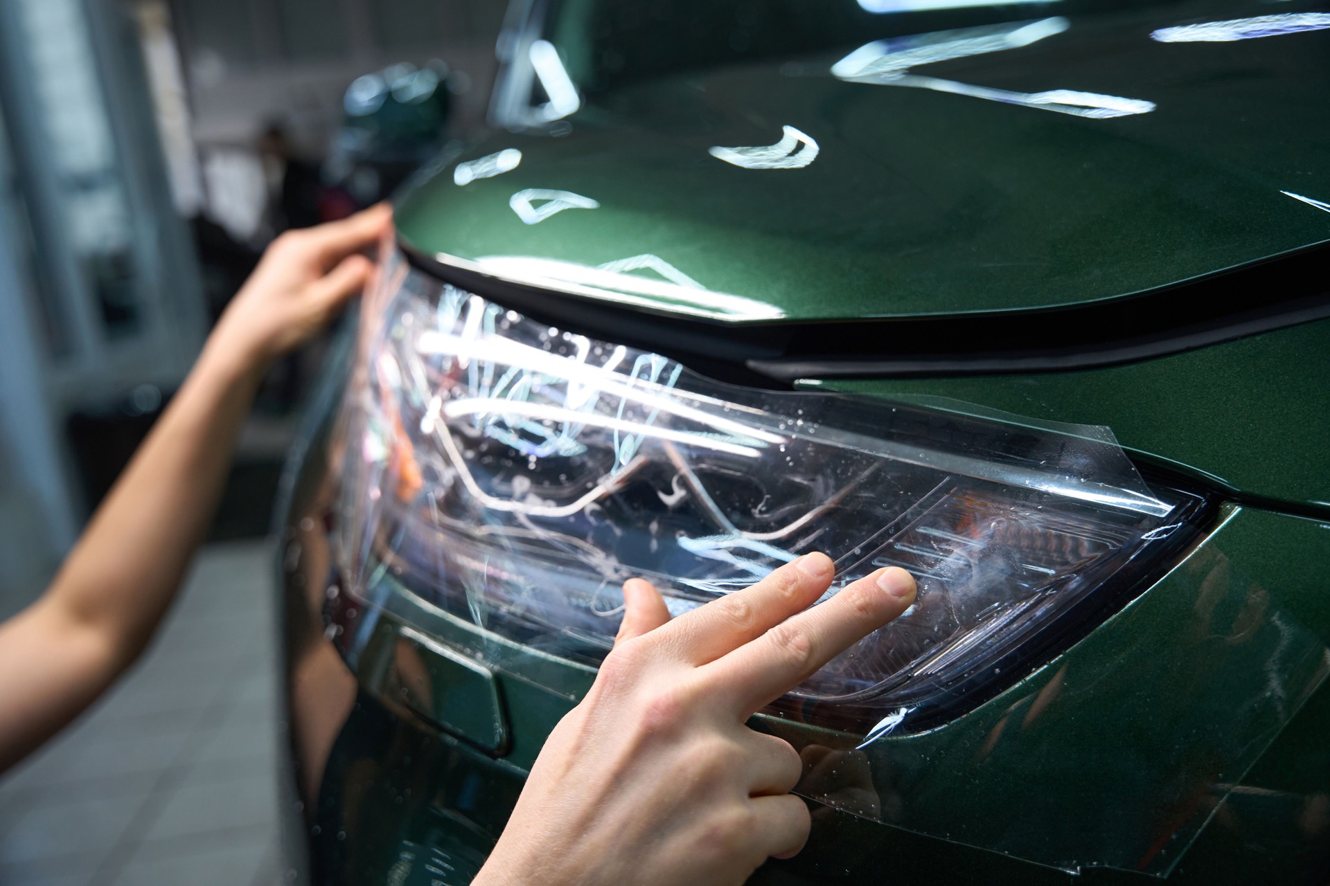 Professional auto detailer is applying protection film to automotive headlight